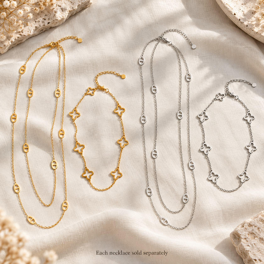 Silver-tone long oval station necklace and short open clover necklace displayed on ivory linen. Each necklace sold separately.
