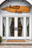 Wooden whale sculpture on a gray wall above a glass door with white curtains.