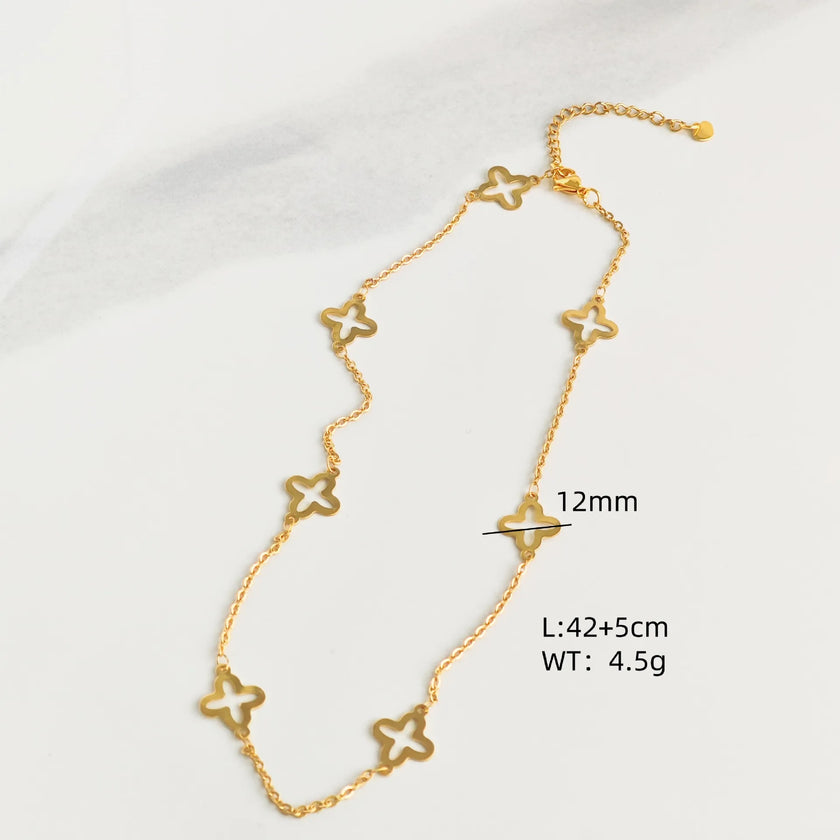 Gold-tone open quatrefoil clover station necklace with extender displayed on ivory linen.