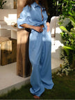 Person wearing a blue outfit standing outdoors with greenery and a white chair in the background