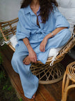 Person wearing a light blue outfit sitting on a wicker chair outdoors.