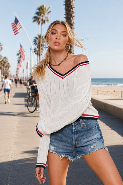 Woman wearing white coastal Americana V-neck sweater with denim shorts on beach boardwalk
